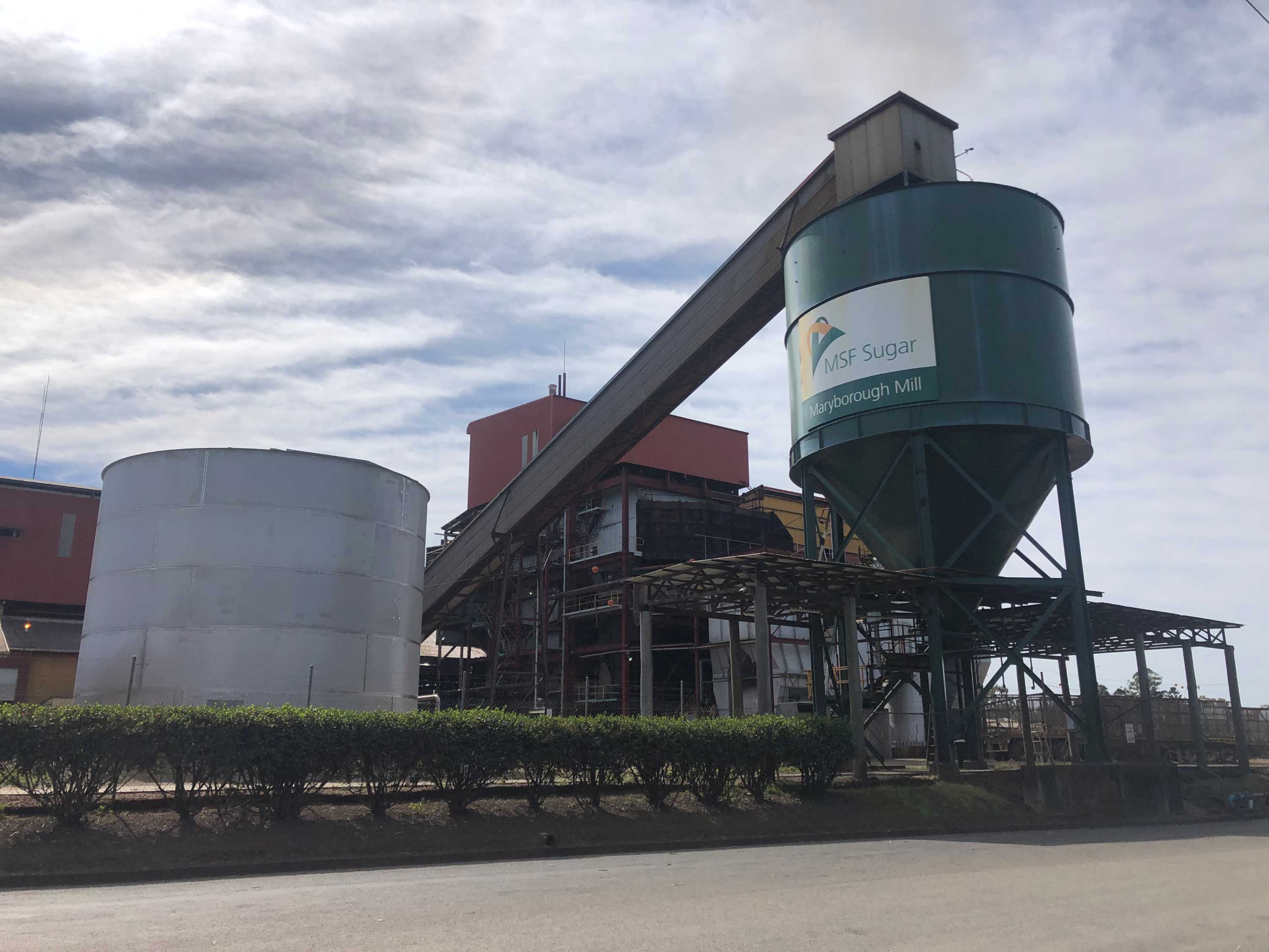 A dark green sugar storage silo with attached escalator at a sugar mill. A sign on the silo says MSF Sugar Maryborough Mill