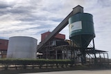 A dark green sugar storage silo with attached escalator at a sugar mill. A sign on the silo says MSF Sugar Maryborough Mill
