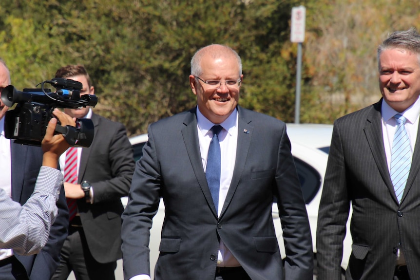 A camera films Scott Morrison and Mathias Cormann in suits as they walk down the road.