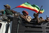 Men with rifles ride in the back of a truck, one man waves an Ethiopian flag.