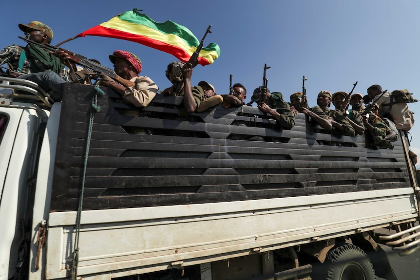 Men with rifles ride in the back of a truck, one man waves an Ethiopian flag.