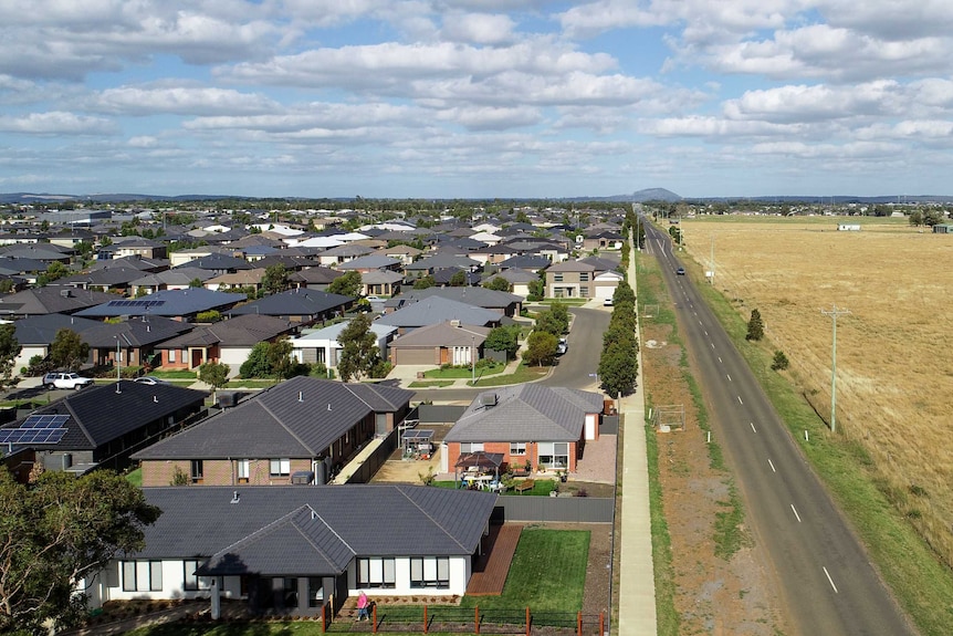 Aerial shot of housing on one side of road, paddocks on the other.