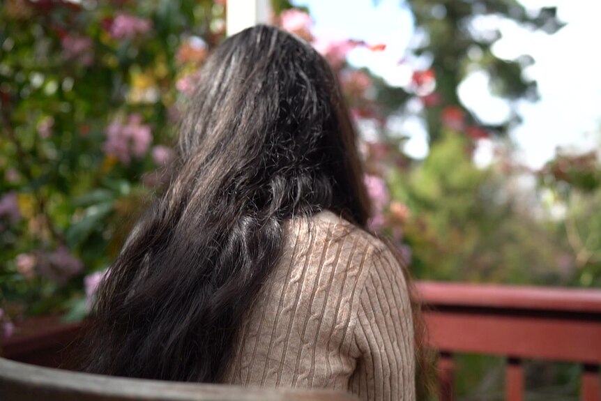 A woman with long dark hair sits outside.