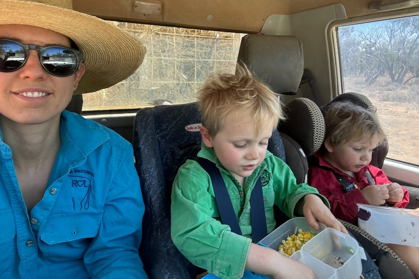 Mum wearing a wide-brimmed hat and her two son eating snacks in their ute