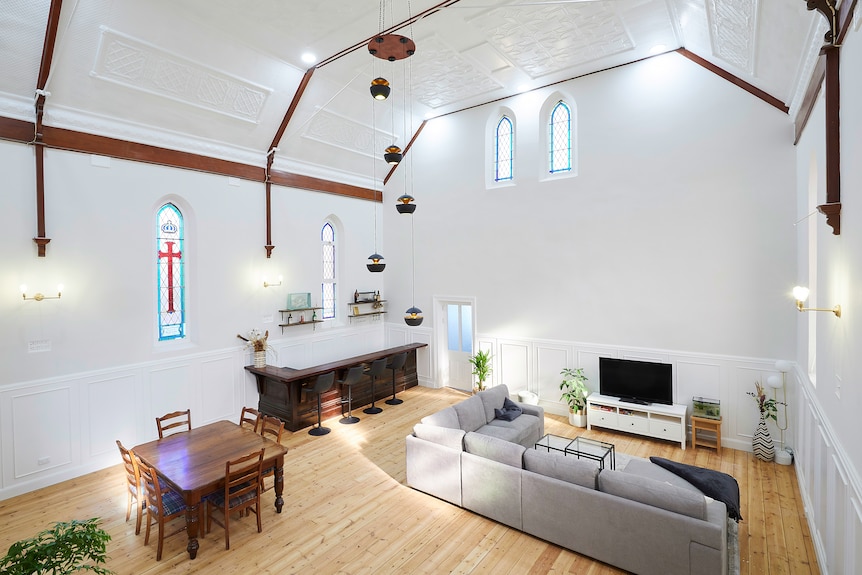 The interior of a church that's been painted white and converted into a living space with couches and a dining table