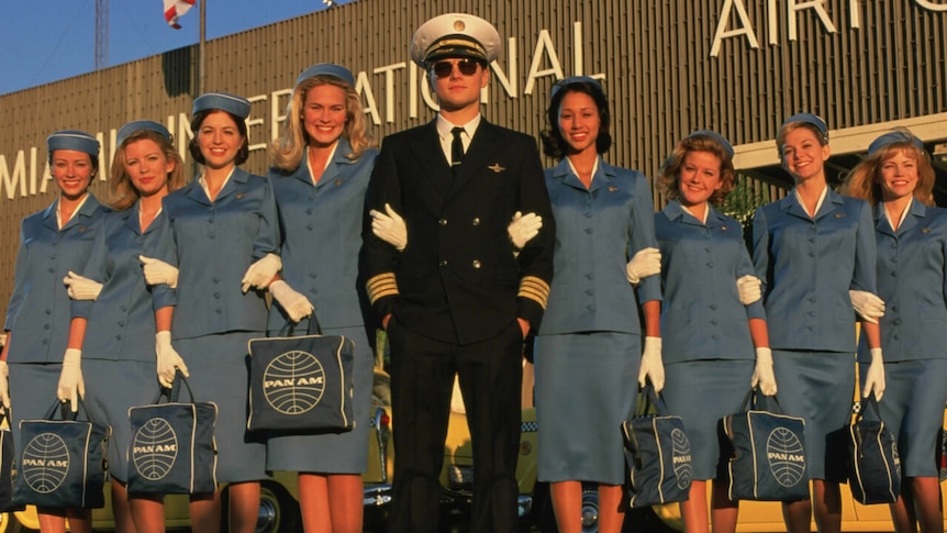 A man in a pilot's uniform flanked by several women in old-style flight attendant uniforms