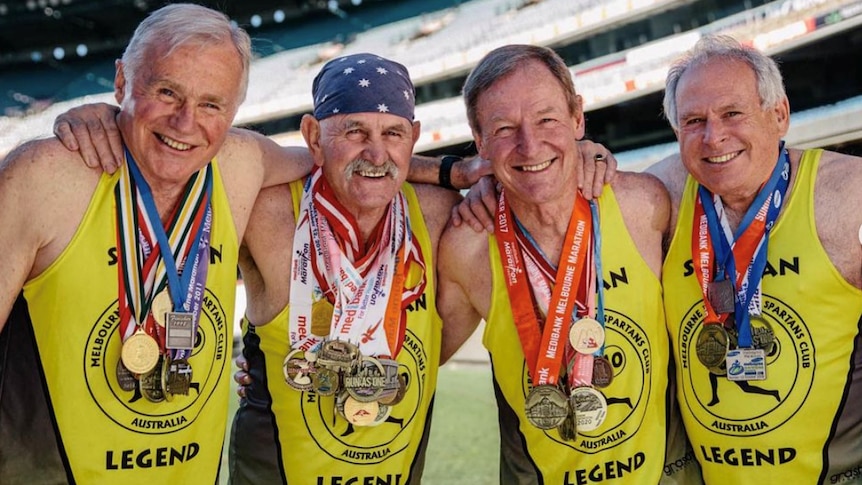 Four of the five older men known as the Spartan Legends, arm in arm and wearing their gold running singlets