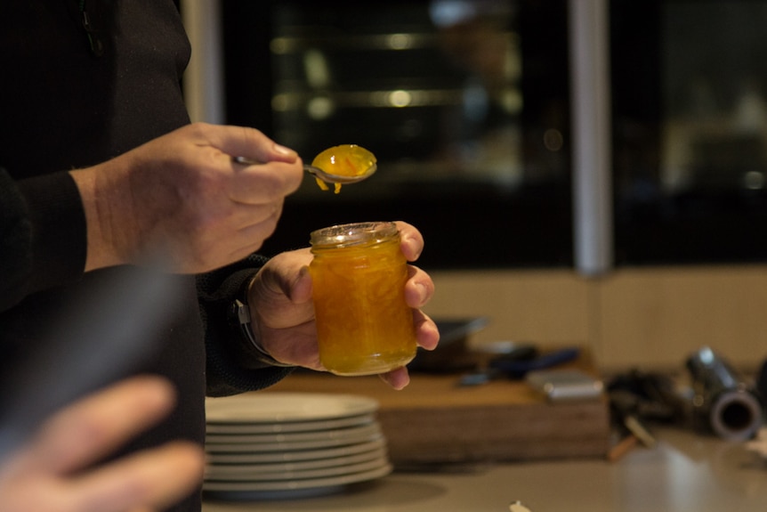 A man spoons marmalade from a jar.