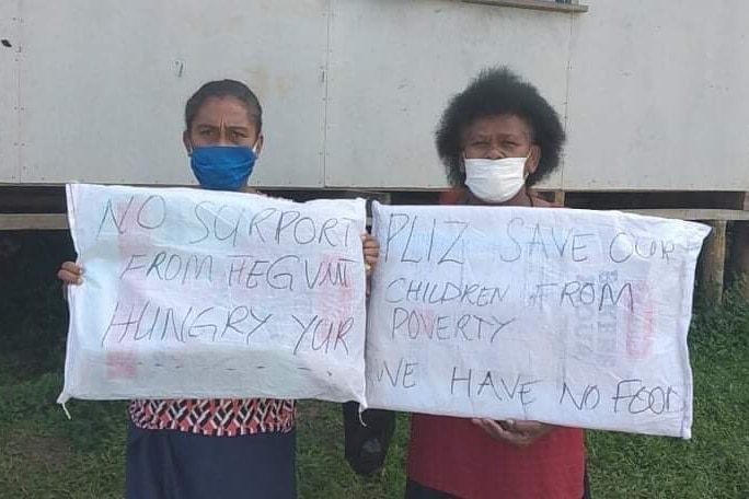 Two women in masks hold up placards.