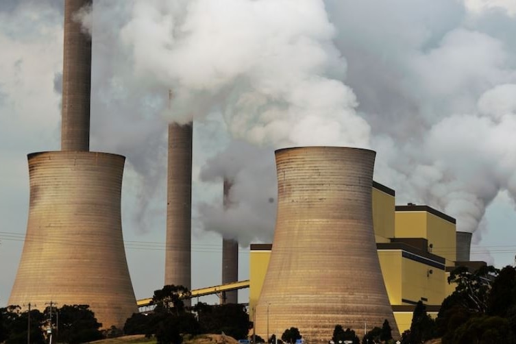 Photo of a power plant, with concrete cylinders and smoke against a grey sky  