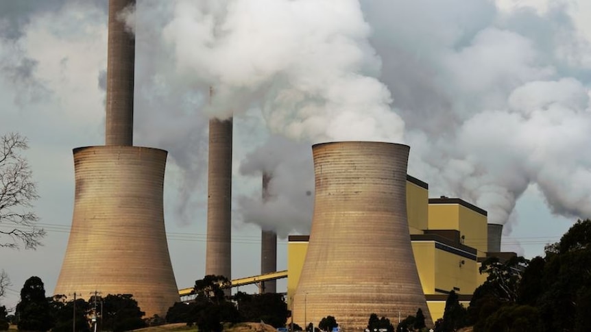 Photo of a power plant, with concrete cylinders and smoke against a grey sky  