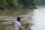 Kham La and his son Kham Ai pilot their dugout canoe along the Mekong.