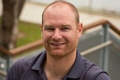 A man wearing a navy polo top looking at the camera and smiling.