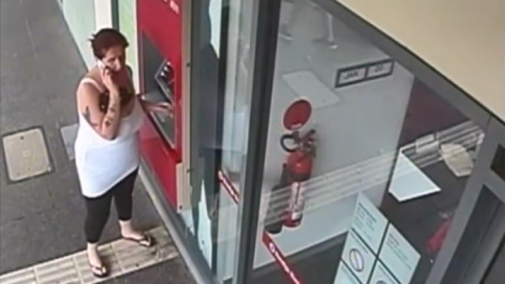 Samantha Kelly speaks on a mobile phone while standing next to an ATM.