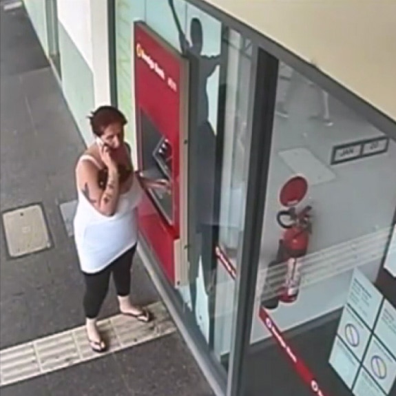 Samantha Kelly speaks on a mobile phone while standing next to an ATM.