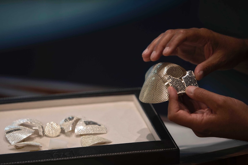 Parts of an unfinished face mask covered in tiny diamonds.