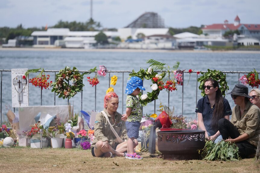 People sit on the Broadwater near floral tributes for Gold Coast helicopter crash victims