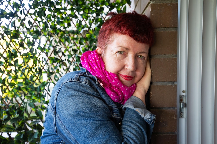 Woman with red hair and pink scarf leans on wall 