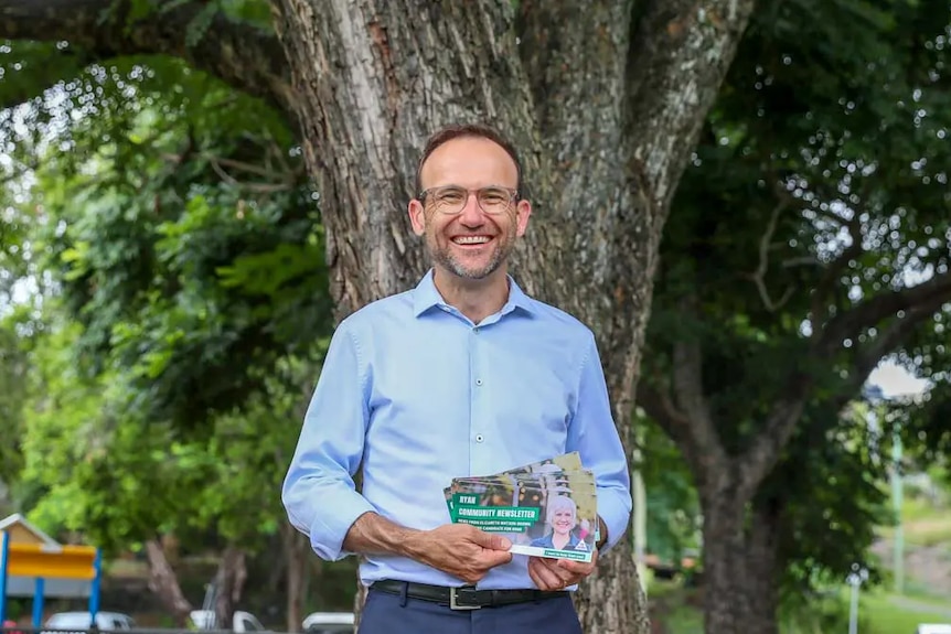Adam Bandt, Vorsitzender der australischen Grünen, hält Werbebroschüren vor einem Baum.