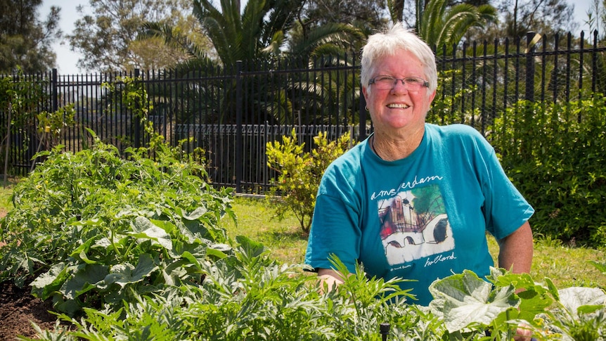 Kerry Cooper kneels next to a garden bed.