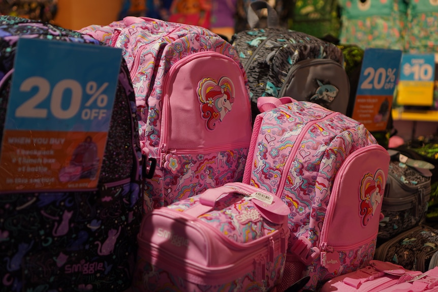 Pink patterned backpacks are stacked next to a 20 per cent off sign.