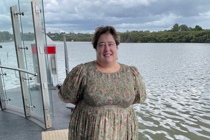 Woman in green floral dress smiles while standing on a ferry.