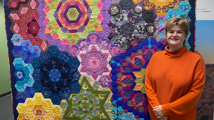 Woman stands next to large colourful quilt