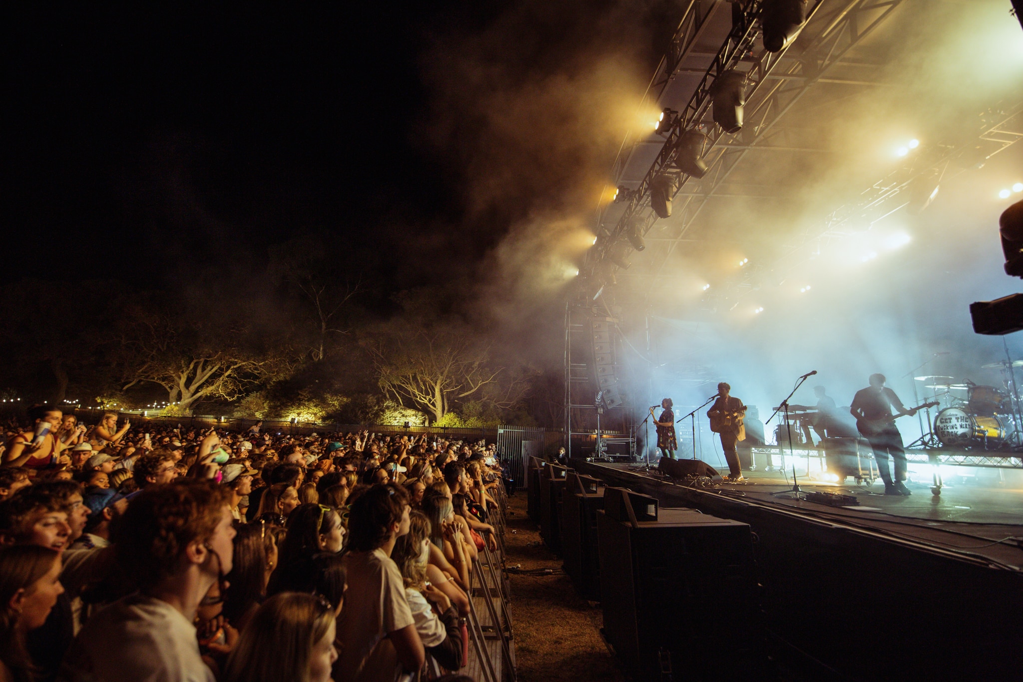 A festival crowd at night taken looking along the front barrier as a band plays on stage