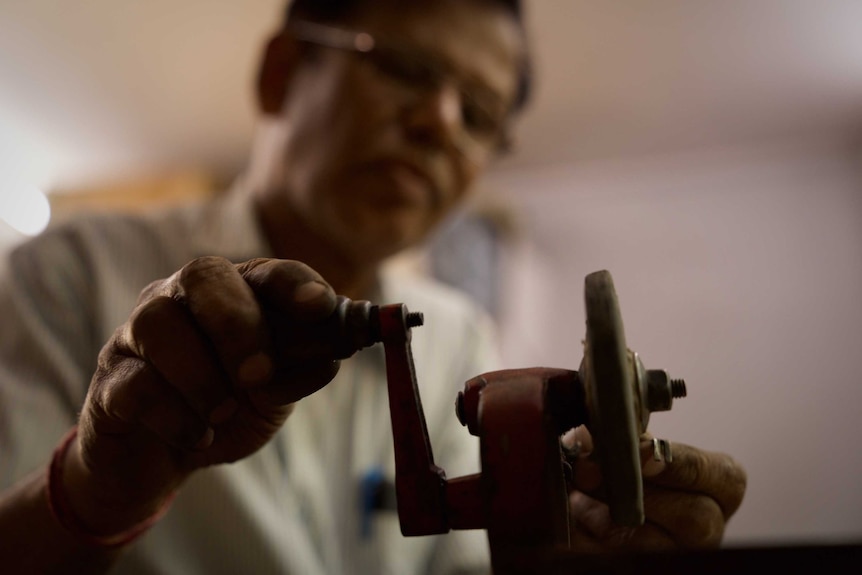 Close view of a man turnin some kind of wheel with a piece of metal pressed against the edge.