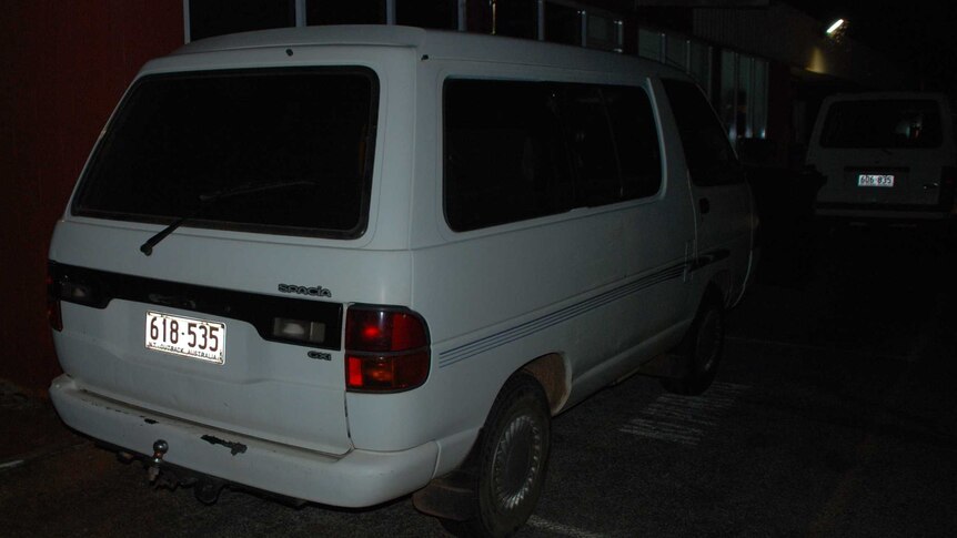 A white van with NT number plates, parked outside a building at night time.