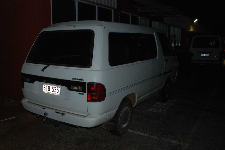 A white van with NT number plates, parked outside a building at night time.