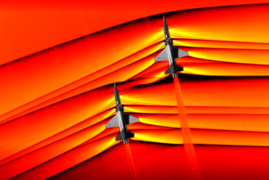 Orange and red shockwaves coming off two jets flying in formation.