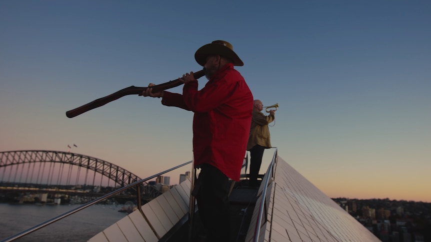Sunet shot of a man playing the didgeridoo on top of the Sydney Opera House.