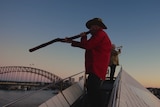 Sunet shot of a man playing the didgeridoo on top of the Sydney Opera House.