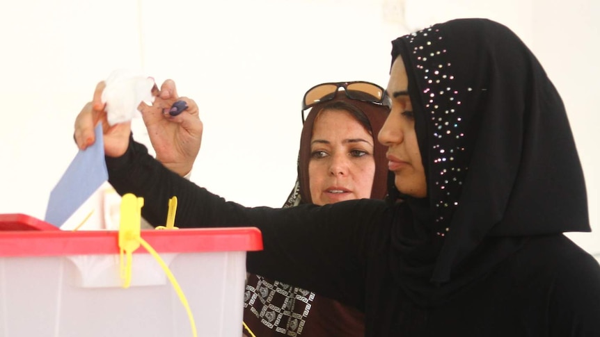Women place their votes in a ballot box.