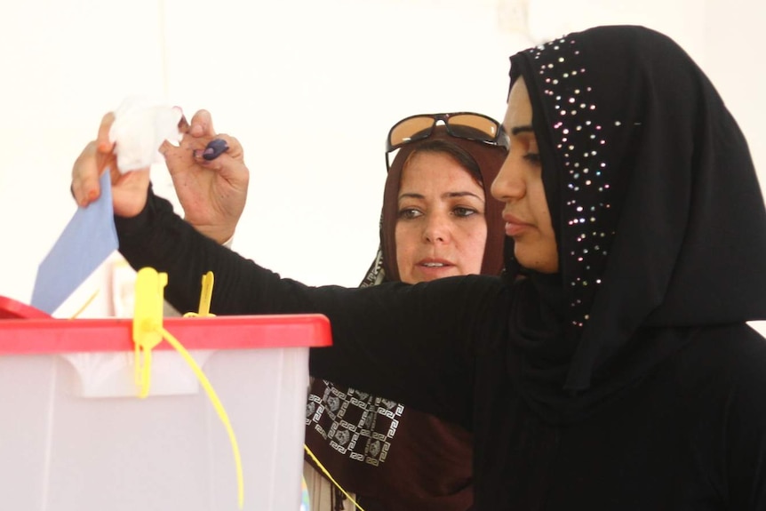 Women place their votes in a ballot box.