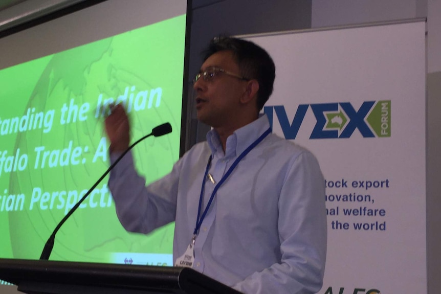 A man with hand raised, addressing a conference, with banners of Livex Forum