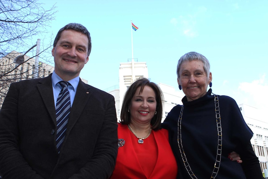Rodney Croome, Sue Hickey and Susan Ditter with rainbow flag over Hobart City Council building.