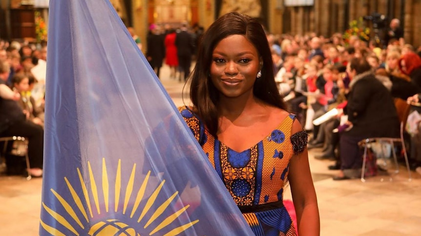 Oluwaseun Ayodeji Osowobi in a traditional African dress holding the flag of Nigeria at Westminster Abbey