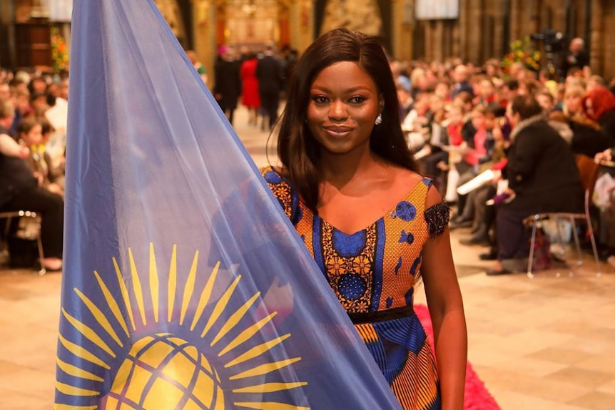 Oluwaseun Ayodeji Osowobi in a traditional African dress holding the flag of Nigeria at Westminster Abbey