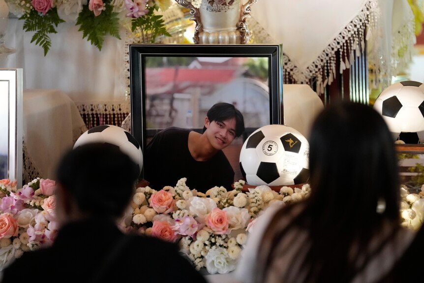 A photo of a boy smiling surrounded by a soccer balla nd flowers.