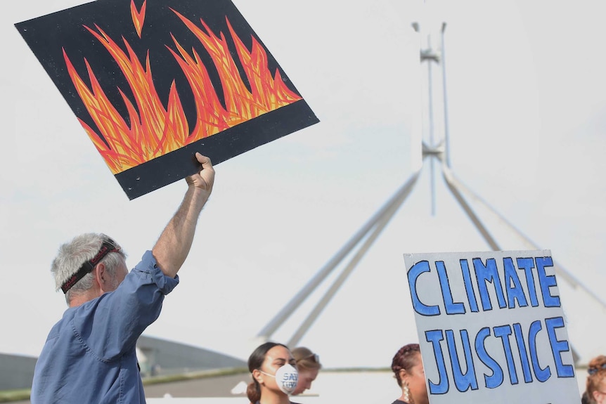 A man stands among protestors, holding a a painting of flames.