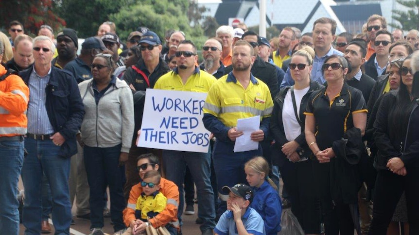 Dozens of people standing outside Parliament House in Perth, one holding a sign saying "workers need their jobs".