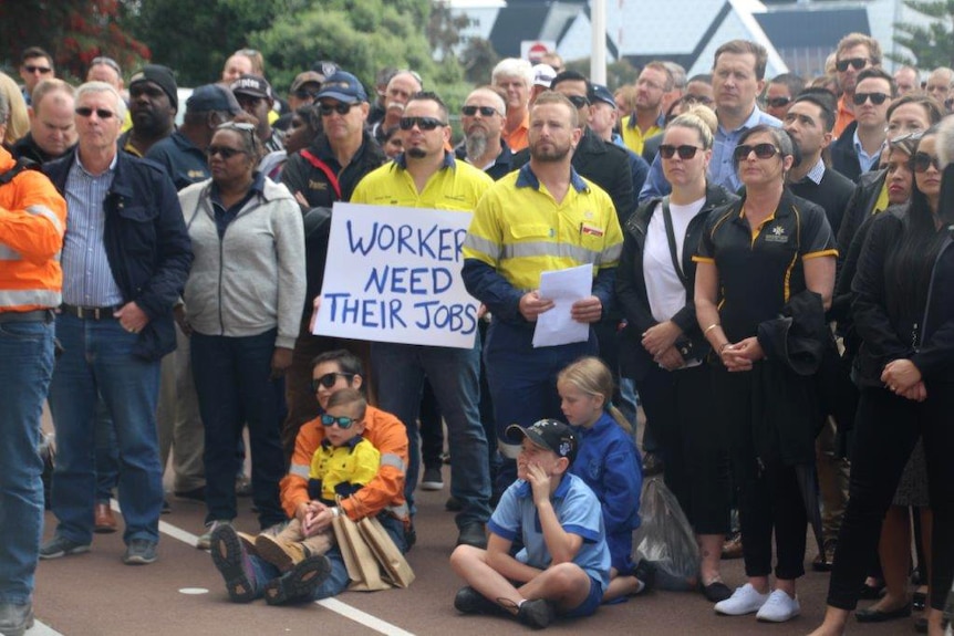 Dozens of people standing outside Parliament House in Perth, one holding a sign saying "workers need their jobs".