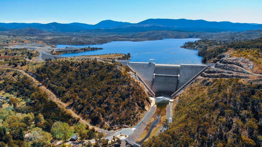 An aerial shot looks over a well-filled dam reservoir.