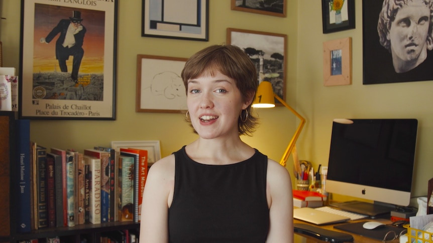 Mary McGillivray, a young woman with a short haircut, sitting in an office filled with books and artwork