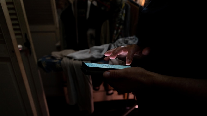 A woman's hands typing on a phone in a dimly lit room. The phone illuminates her hands.