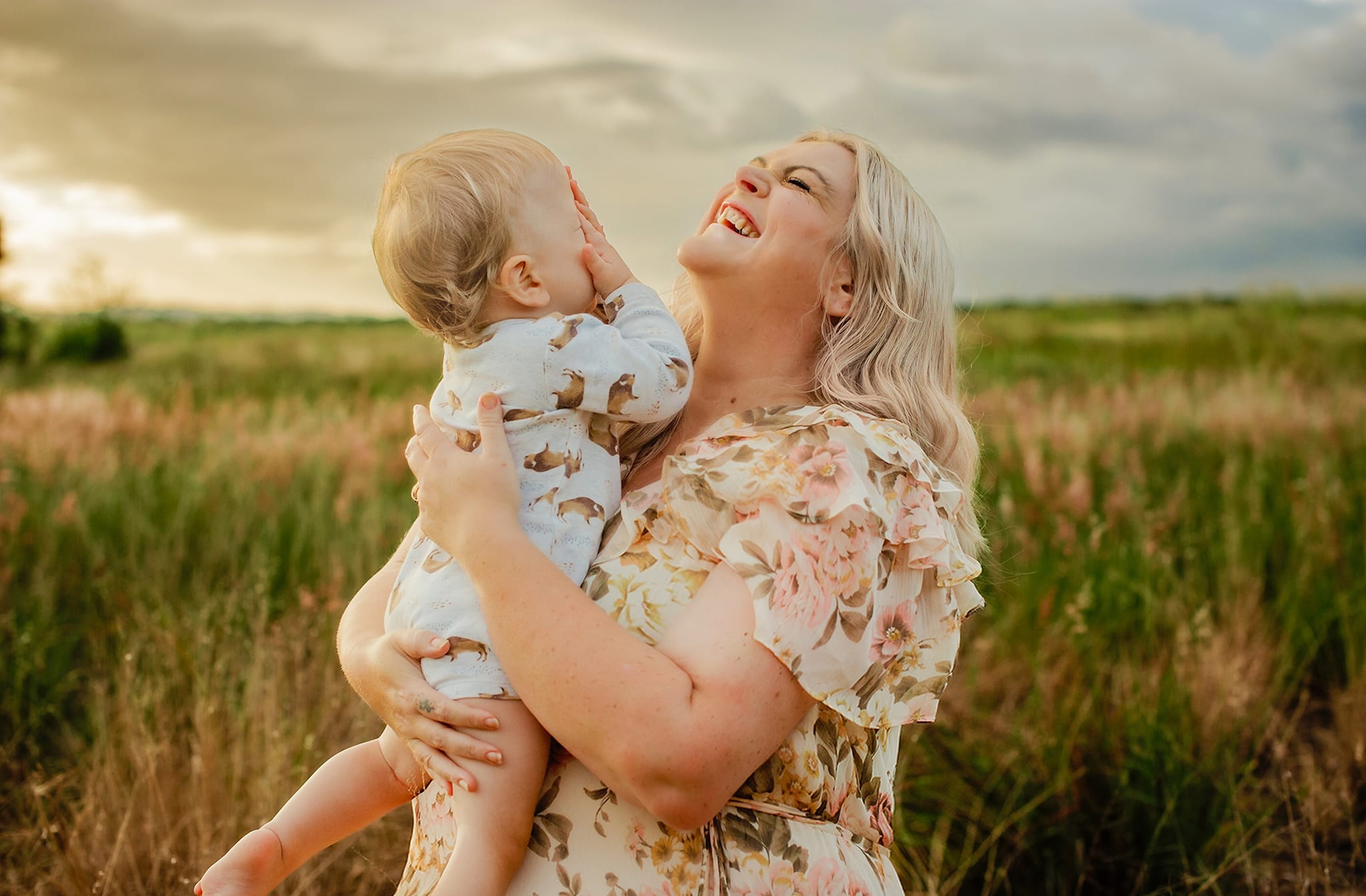 Amanda Wright smiling and holding her baby son in a grassy field at goldenhour.