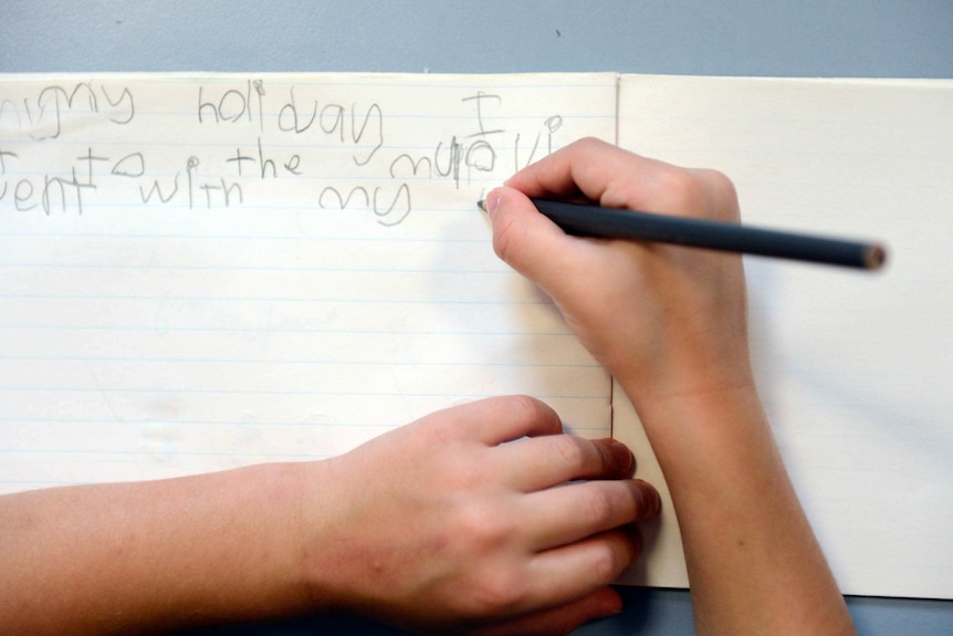 An overhead shot shows a young child writing in an exercise book