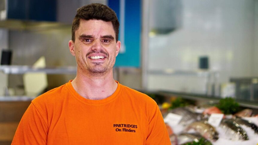 Brown-haired man standing in seafood shop.